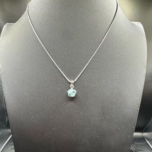 Round light blue crystal incased in a silver square on a silver chain.